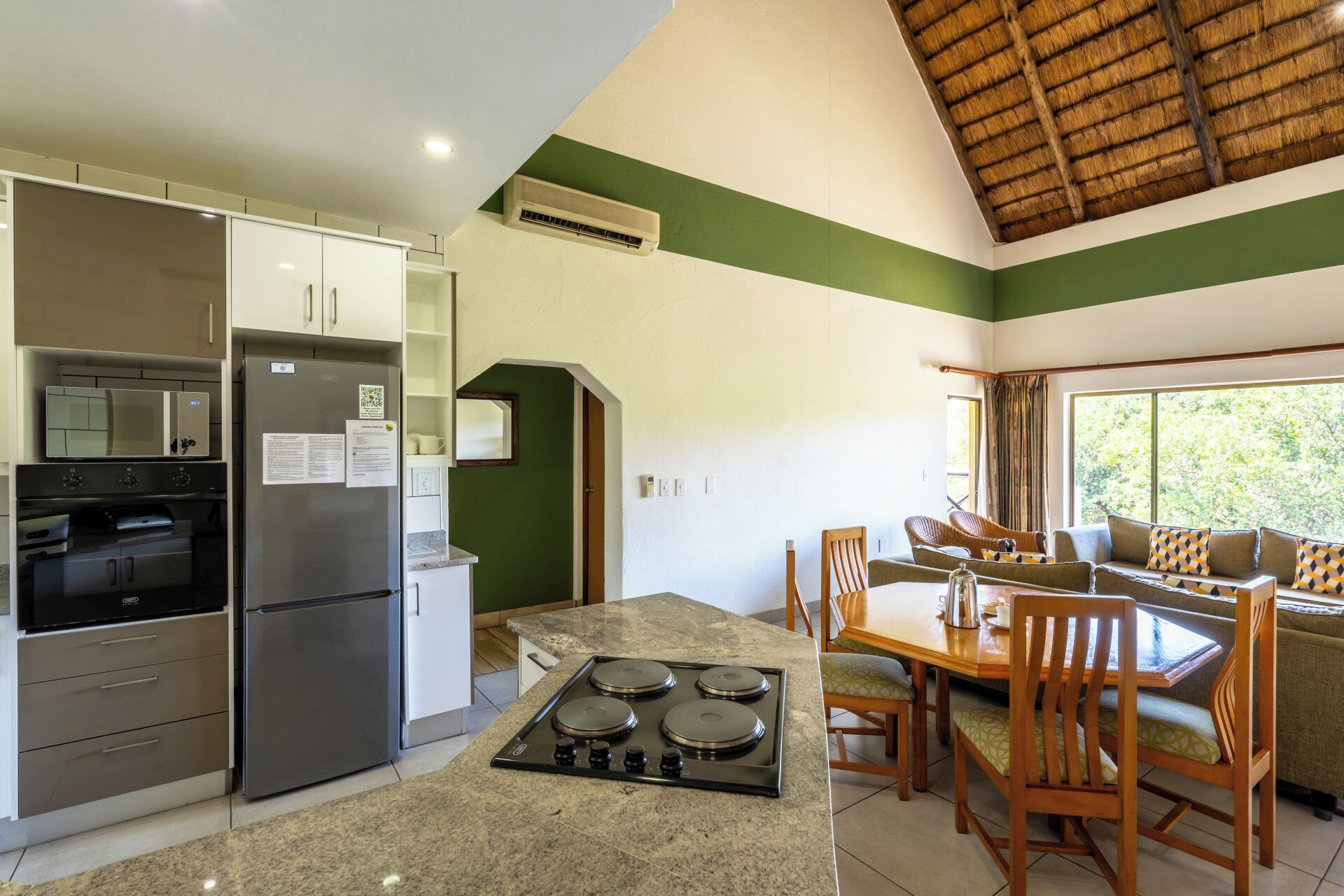 Una cocina compacta con horno integrado, un refrigerador y estufa a gas. Hay una zona de comedor con una mesa y sillas.