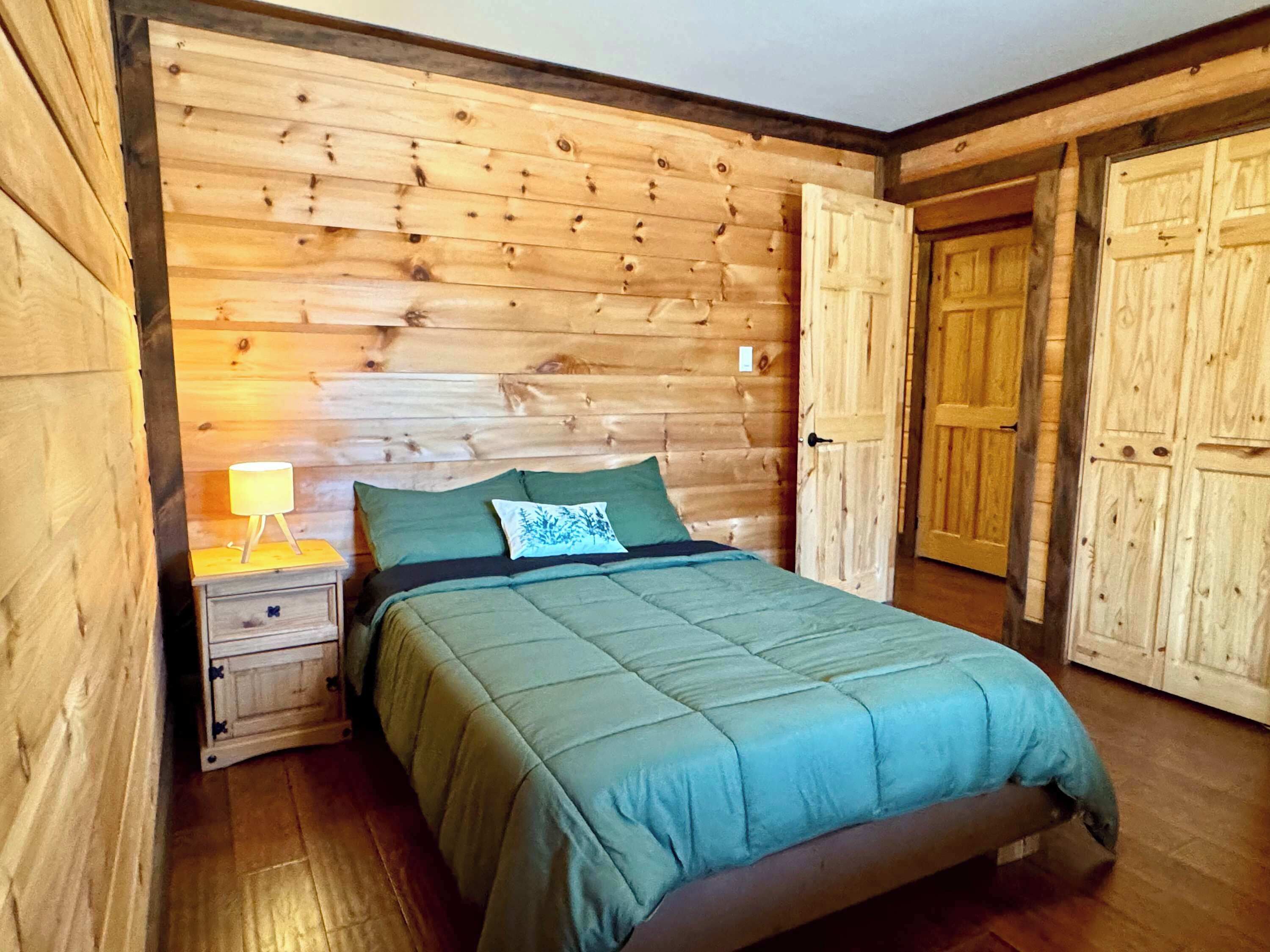 Een slaapkamer met houten lambrisering, een bed, nachtkastje en twee deuren.
