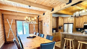 Un intérieur en bois comprenant une table à manger, des chaises, un lustre et un coin cuisine.