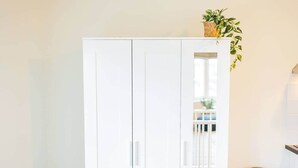 Un armario blanco de dos puertas, una planta pequeña encima y un bote de basura a su lado.