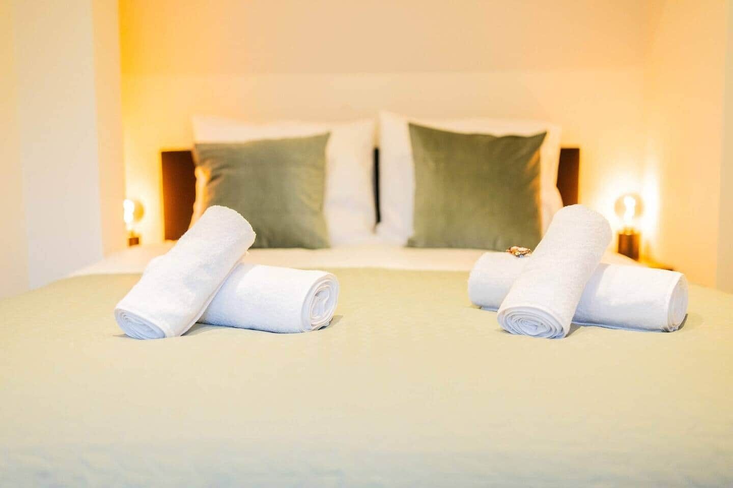 A hotel room with a neatly made bed, two pillows, and two bedside lamps.
