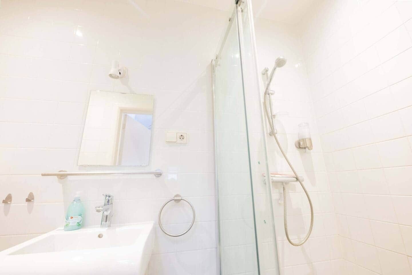 A bathroom with a glass-enclosed shower, a sink, a mirror, and a soap dispenser.