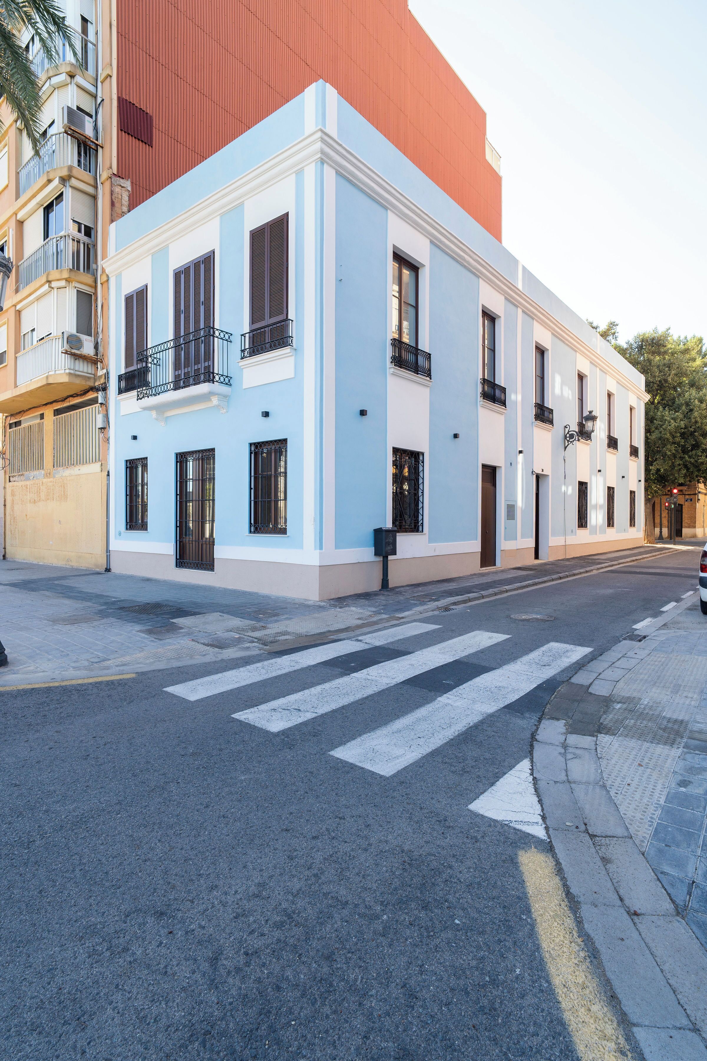 Un edificio azul claro con fachada blanca, múltiples ventanas y balcones.