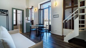 A modern hotel room with a bed, a dining area with a table and chairs, a staircase, and a view of the outdoors. - VLC Host - Reina  (Valencia)