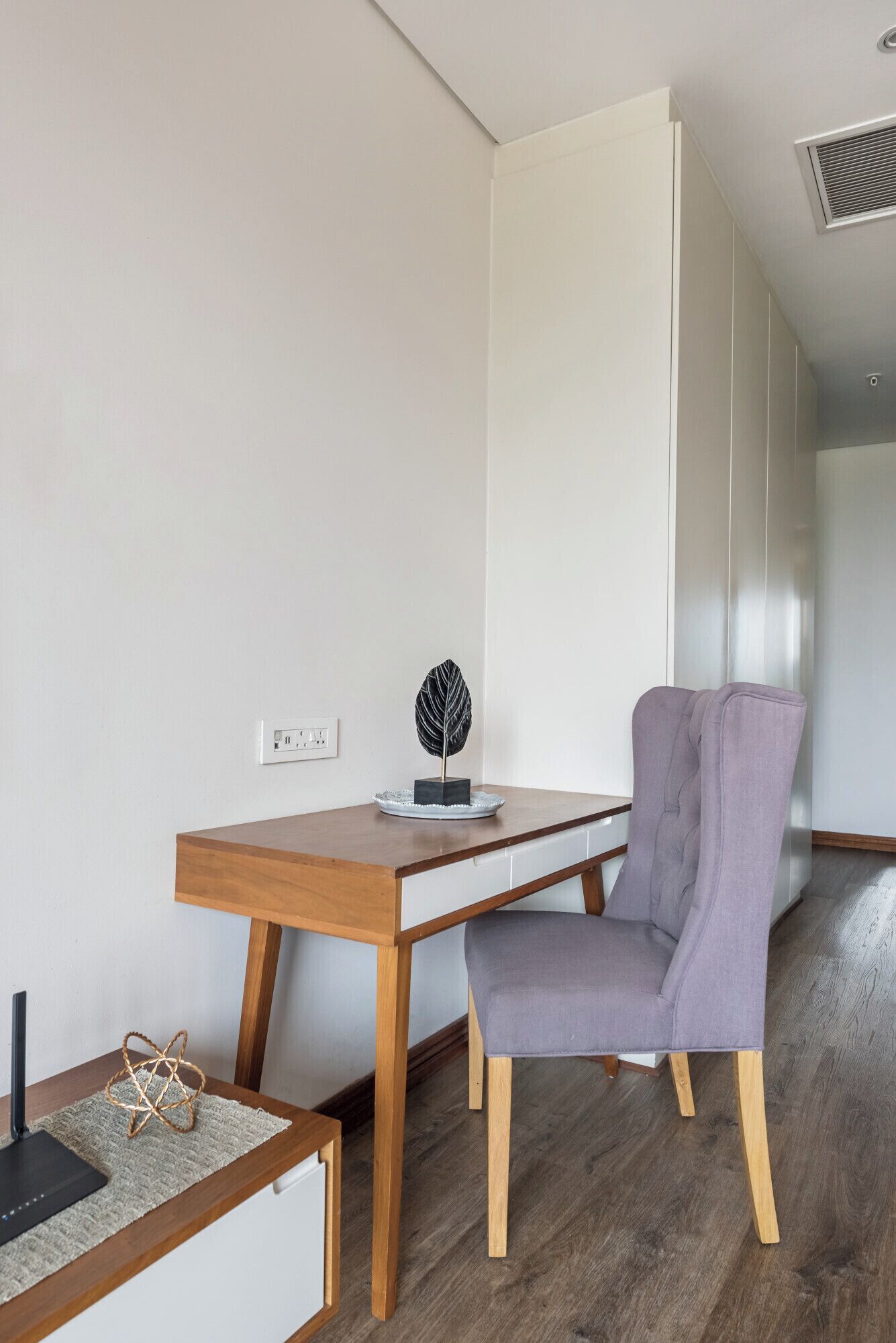 A modern, minimalist room with a wooden desk, a grey upholstered chair, and a decorative leaf sculpture.