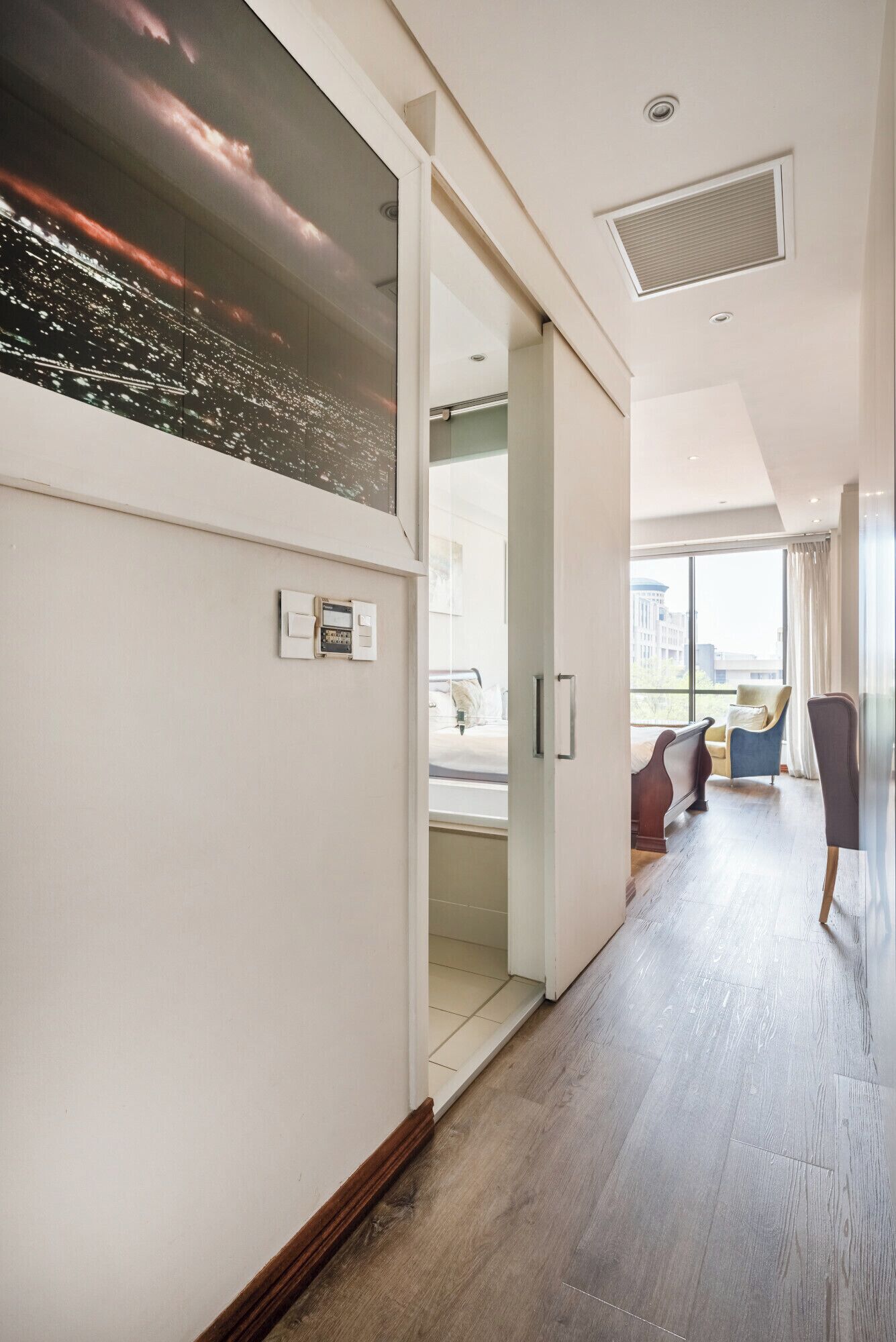 A hotel room with a large window, a bed, a chair, and a bedside table.