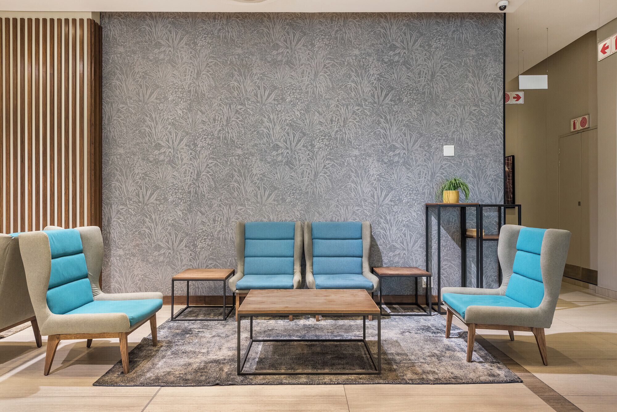 Un vestíbulo con pared estampada, dos sillones azules, una mesa de centro de madera y una mesita con una planta.