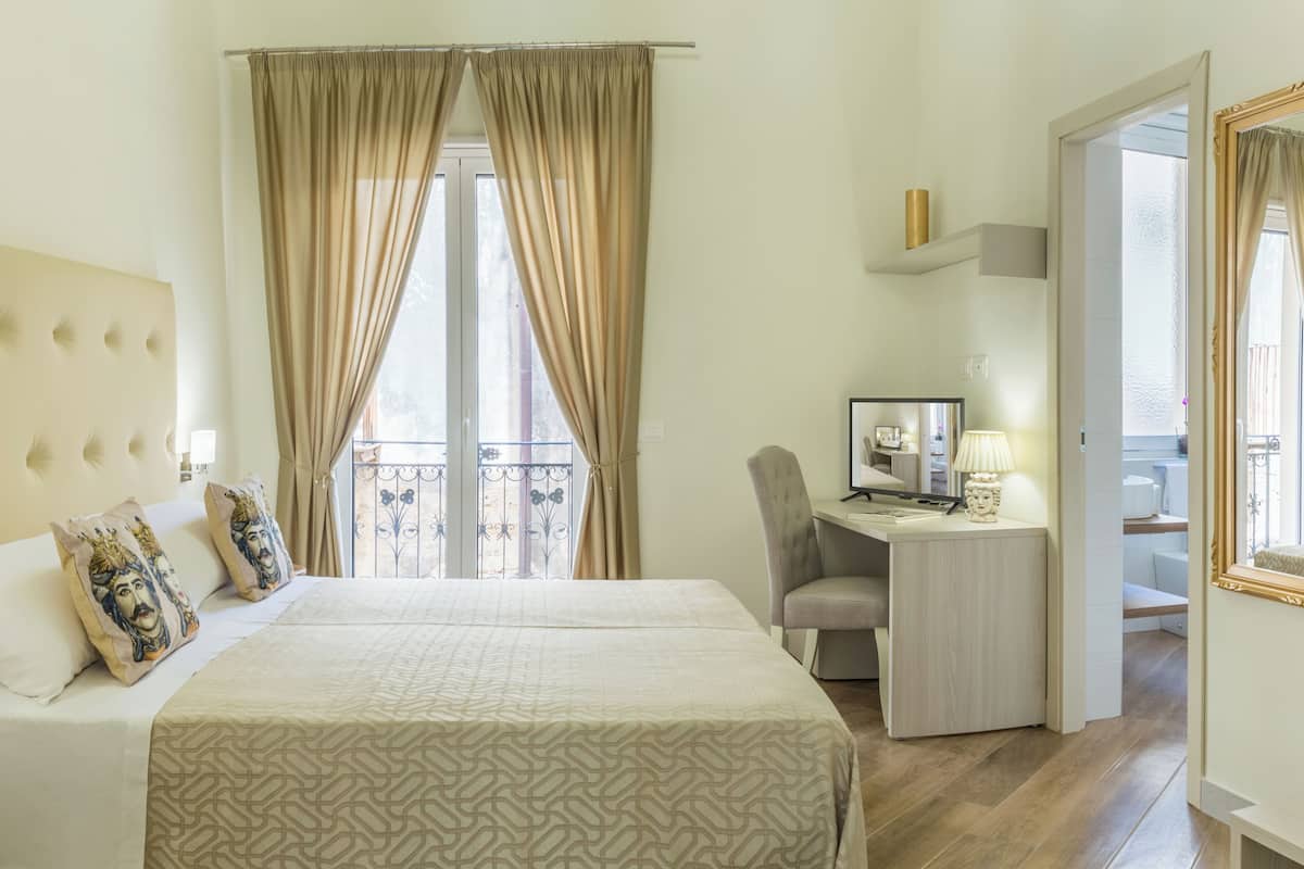 Ein Hotelzimmer mit Bett, Schreibtisch, Stuhl, Fernseher und einem Balkon mit Geländer.