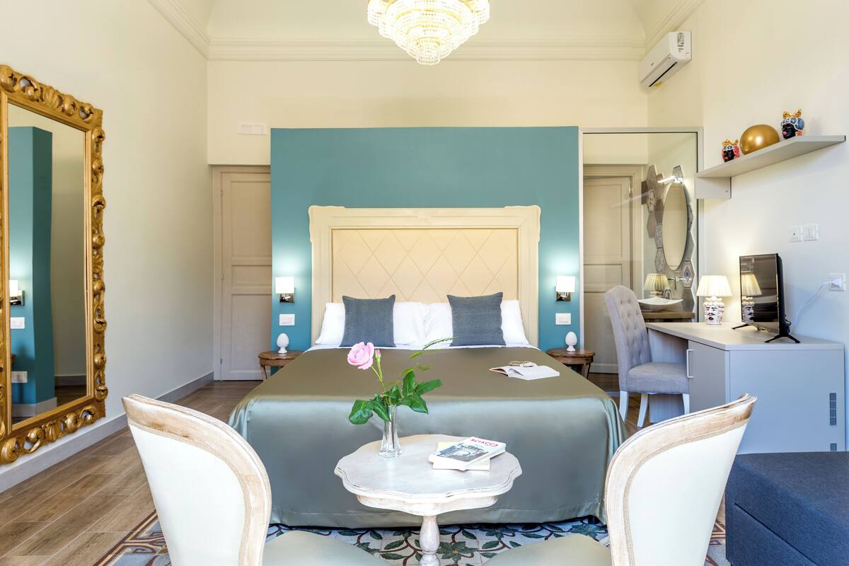 Ein Hotelzimmer mit einem großen Bett, einem Schreibtisch, einem Sessel, einem kleinen Tisch mit Blumen und einem Spiegel.