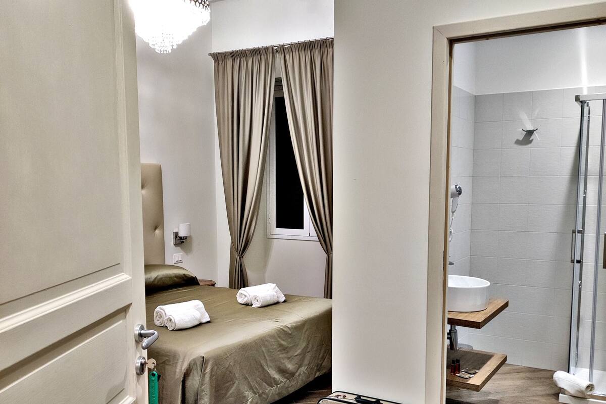 Ein Hotelzimmer mit Bett, Dusche, Koffer und Pendelleuchte.