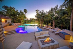 Un área de piscina con sillones de descanso, una chimenea y un pequeño edificio.