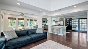 A spacious living area with a dark leather sofa, a patterned rug, and a kitchen in the background. - Luxury Sanctuary Retreat-Heated pool-Hot tub-Volleyball (Encinitas)