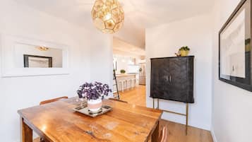 A dining area with a wooden table, chairs, a vase of flowers, a pendant light, and a black cabinet with a chevron pattern.