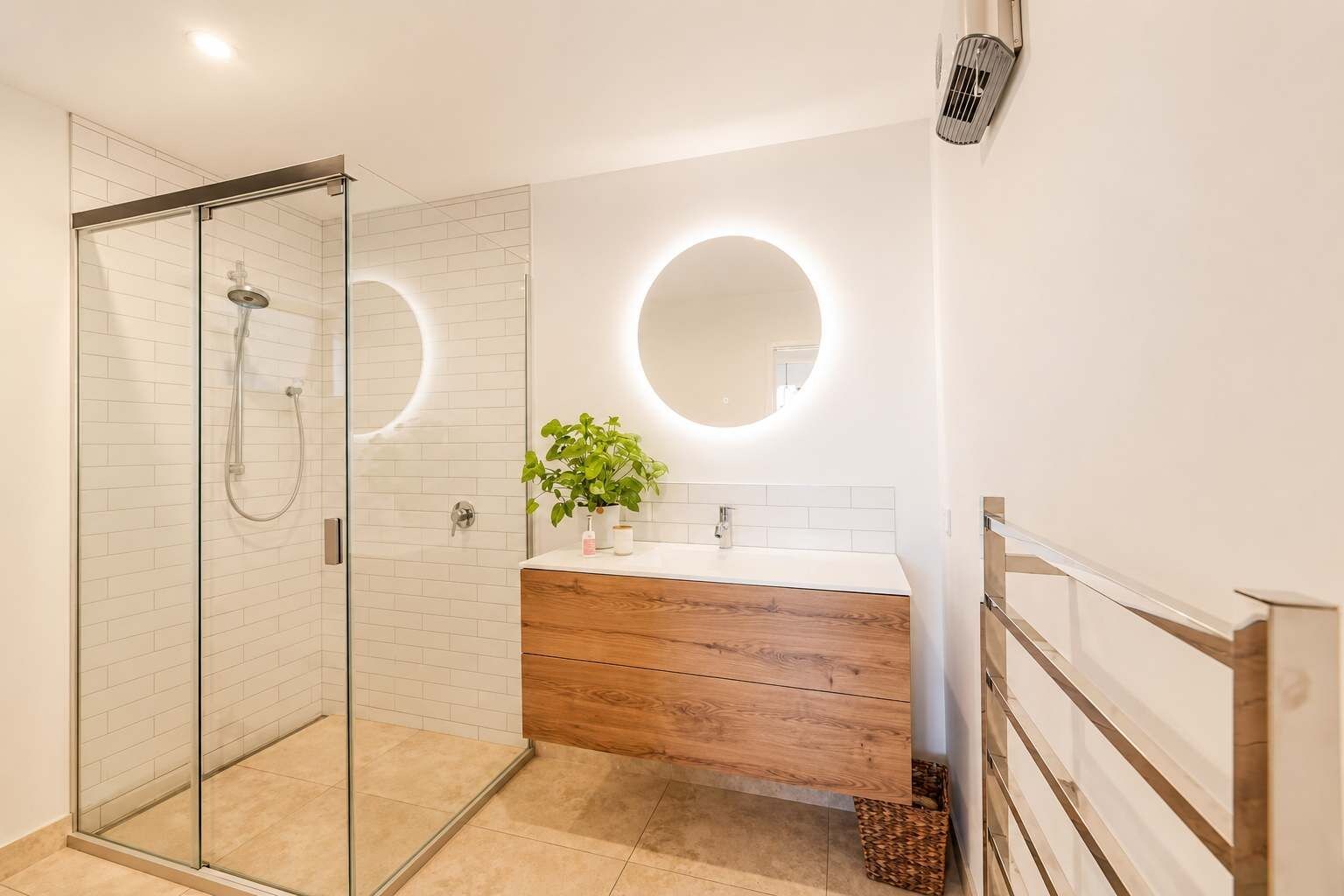 Un bagno moderno con cabina doccia in vetro, un mobile bagno in legno e uno specchio rotondo.