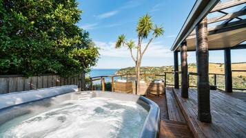 Un jacuzzi en una terraza de madera con vista al océano y palmeras.