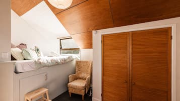 A bedroom with a wooden ceiling, a bed with floral bedding, a chair, a wooden bench, and a wardrobe.