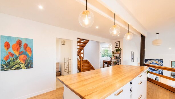 A modern kitchen with a wooden island, pendant lights, and a staircase leading to another room.