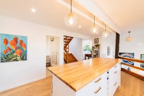 A modern kitchen with a wooden island, pendant lights, and a staircase leading to another room.