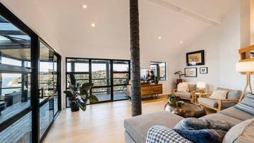 Amplia sala de estar con un ventanal, piso de madera, un sofá, una mesa de centro y vistas al exterior.
