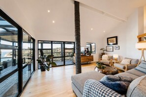 A spacious living room with a large window, a wooden floor, a sofa, a coffee table, and a view of the outdoors.