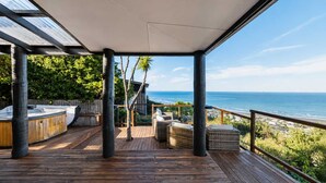 A wooden deck with outdoor seating, a view of the ocean, and a covered area with a glass ceiling.