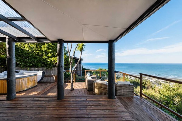 A wooden deck with outdoor seating, a view of the ocean, and a covered area with a glass ceiling.