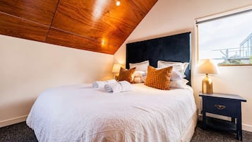 A hotel room with a large bed, a dark headboard, a nightstand with a lamp, and a view of the outside through a window.