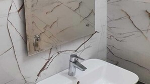 A bathroom with a white sink, a mirror, and marble-patterned walls. - RBS Hotel And Lawn (Faizabad)