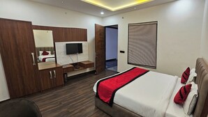 A modern hotel room with a bed, a desk with a TV, a wardrobe, and a ceiling fan. - RBS Hotel And Lawn (Faizabad)