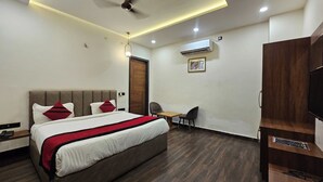 A hotel room with a bed, a desk, a chair, a TV, and an air conditioning unit. - RBS Hotel And Lawn (Faizabad)