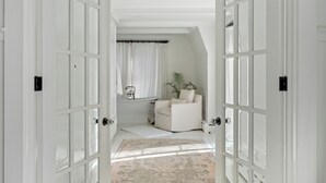 A room with a large window, a white chair, a small table, and a rug. - Lakeview Bliss - Beautifully Decorated Home! Close Private Beach! (Harbor Springs)