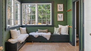 A cozy room with a built-in bench, large windows, and framed botanical prints. - Lakeview Bliss - Beautifully Decorated Home! Close Private Beach! (Harbor Springs)