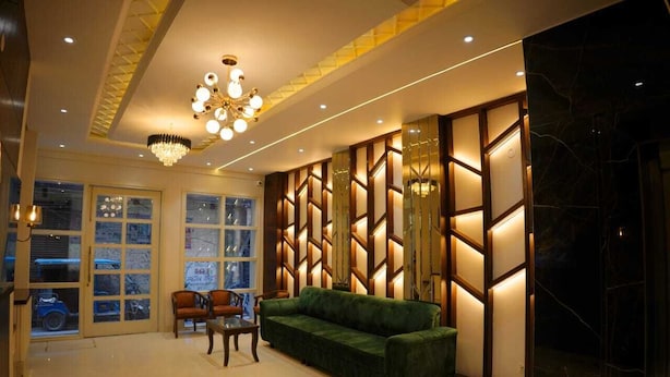 A modern lobby with a green sofa, wooden panel wall, and a chandelier. - Hotel Swastik (Amritsar)