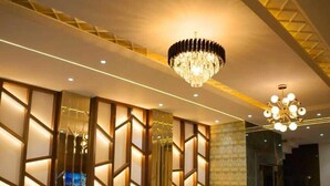 A modern lobby with a green sofa, a glass coffee table, and a chandelier. - Hotel Swastik (Amritsar)