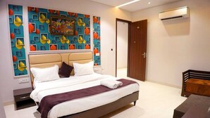A modern bedroom with a bed, a wall with a colorful leaf pattern, a wooden door, and an air conditioning unit. - Hotel Swastik (Amritsar)