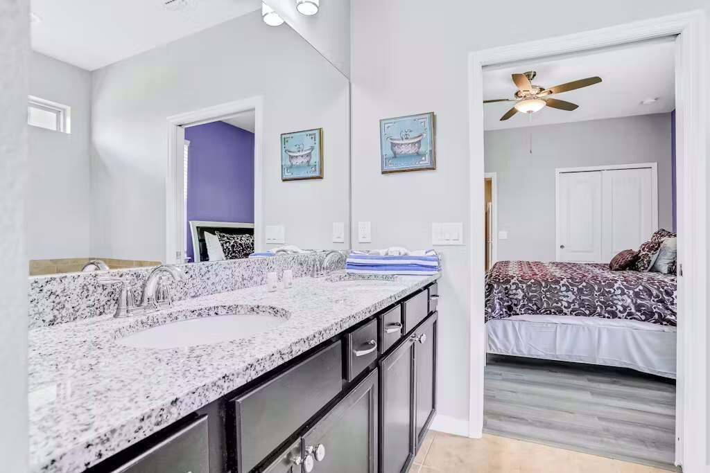 A bathroom with a double sink, dark cabinets, and a ceiling fan.