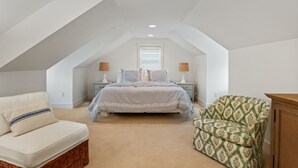 Un dormitorio con cama, dos mesitas de noche, una silla y una mesita auxiliar.
