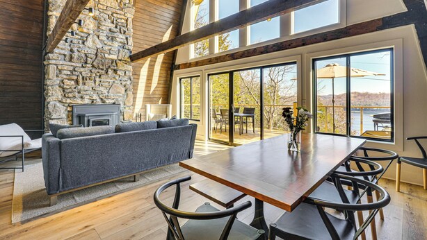 A spacious living area with a stone fireplace, a large wooden dining table, and a view of the outdoors. - Fish, Swim & Kayak: Spacious Beaver Lake Home! (Garfield)