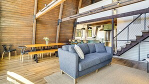 A spacious room with a high ceiling, wooden beams, a sofa, a dining table, and a staircase. - Fish, Swim & Kayak: Spacious Beaver Lake Home! (Garfield)