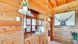 A wooden interior with a counter displaying framed pictures, a hanging light fixture, and a large bull's head painting. - Mtn-view Cabin w/ Horse Pasture in Koosharem (Koosharem)