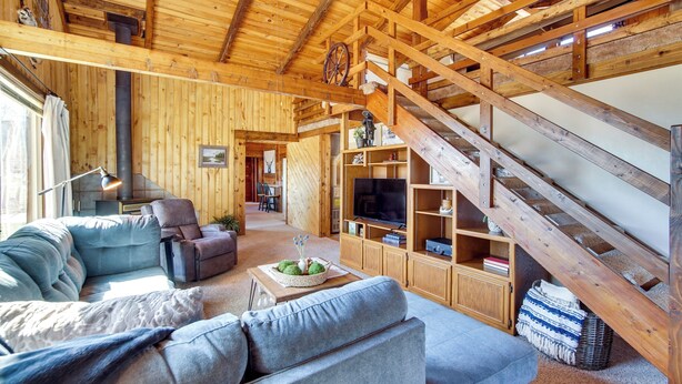 A rustic wooden interior with a sofa, armchair, TV, and a staircase. - Mtn-view Cabin w/ Horse Pasture in Koosharem (Koosharem)