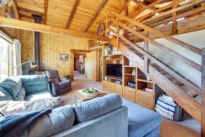 A rustic wooden interior with a sofa, armchair, TV, and a staircase.