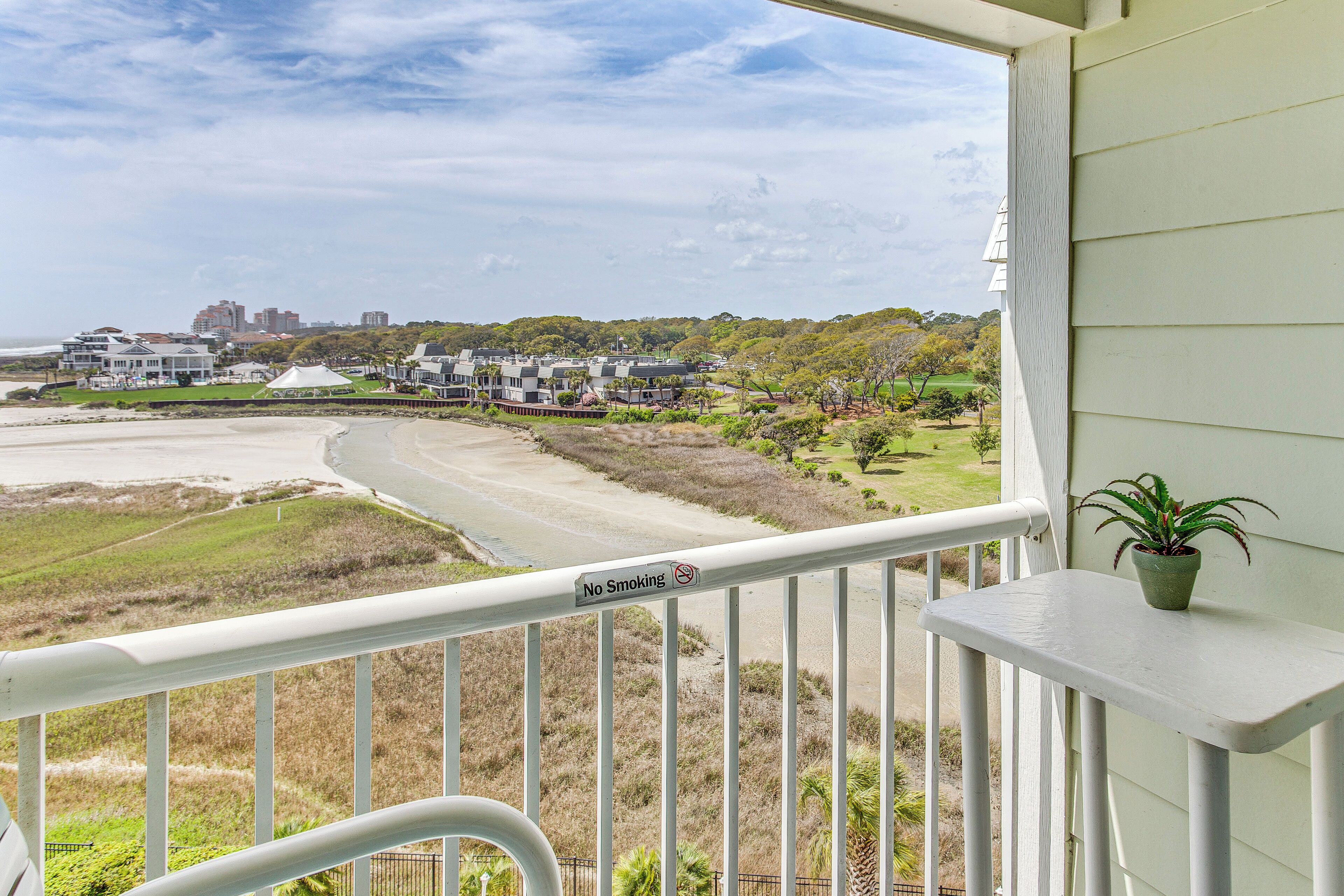 Un balcon orné d’un panneau « Il est interdit de fumer », donnant sur une plage et une zone résidentielle avec des maisons et de la verdure.