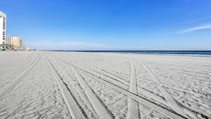 En strand med tydelige dækspor og en klar, blå himmel.