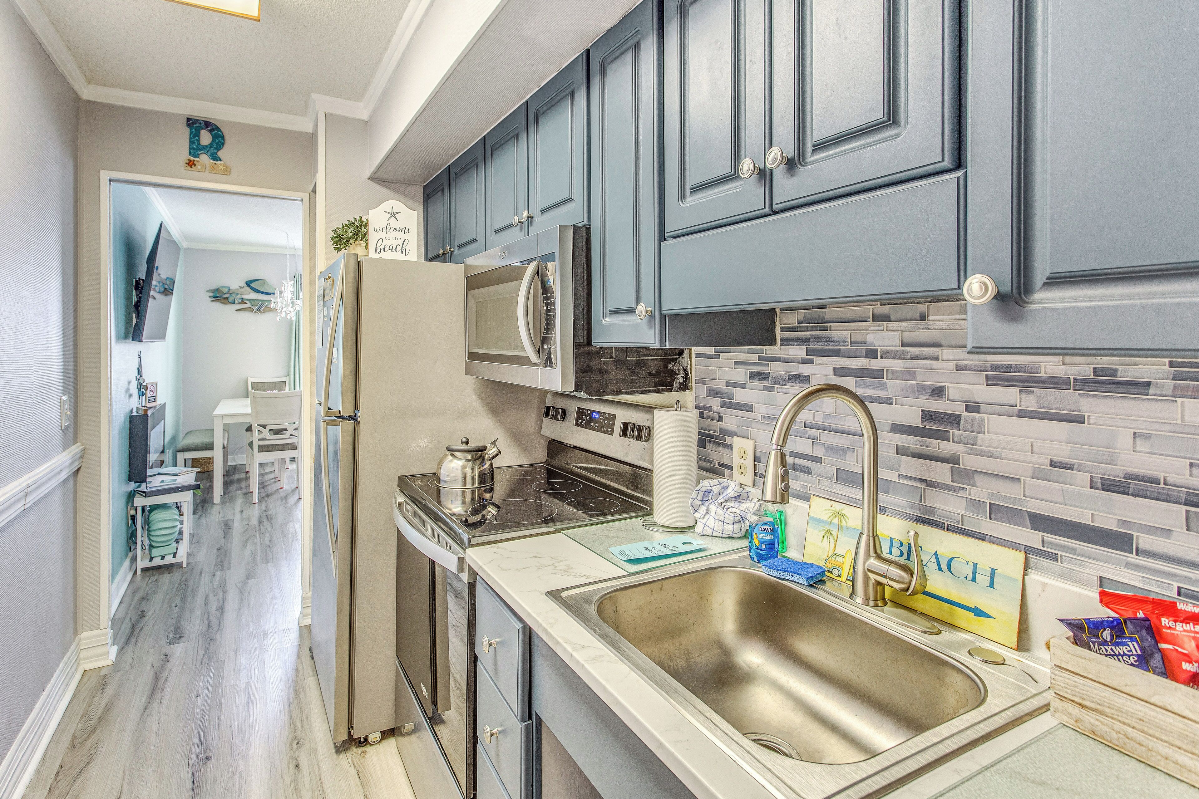 A modern kitchen with grey cabinets, a stainless steel sink, and a tiled backsplash.