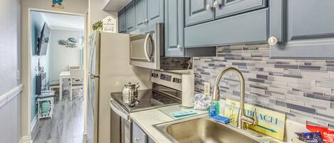 A modern kitchen with grey cabinets, a stainless steel sink, and a tiled backsplash.