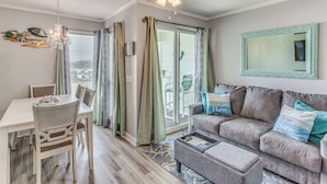 En stue med spiseplads, en grå sofa, en loftsvifte og en skydedør, der fører ud til en balkon.