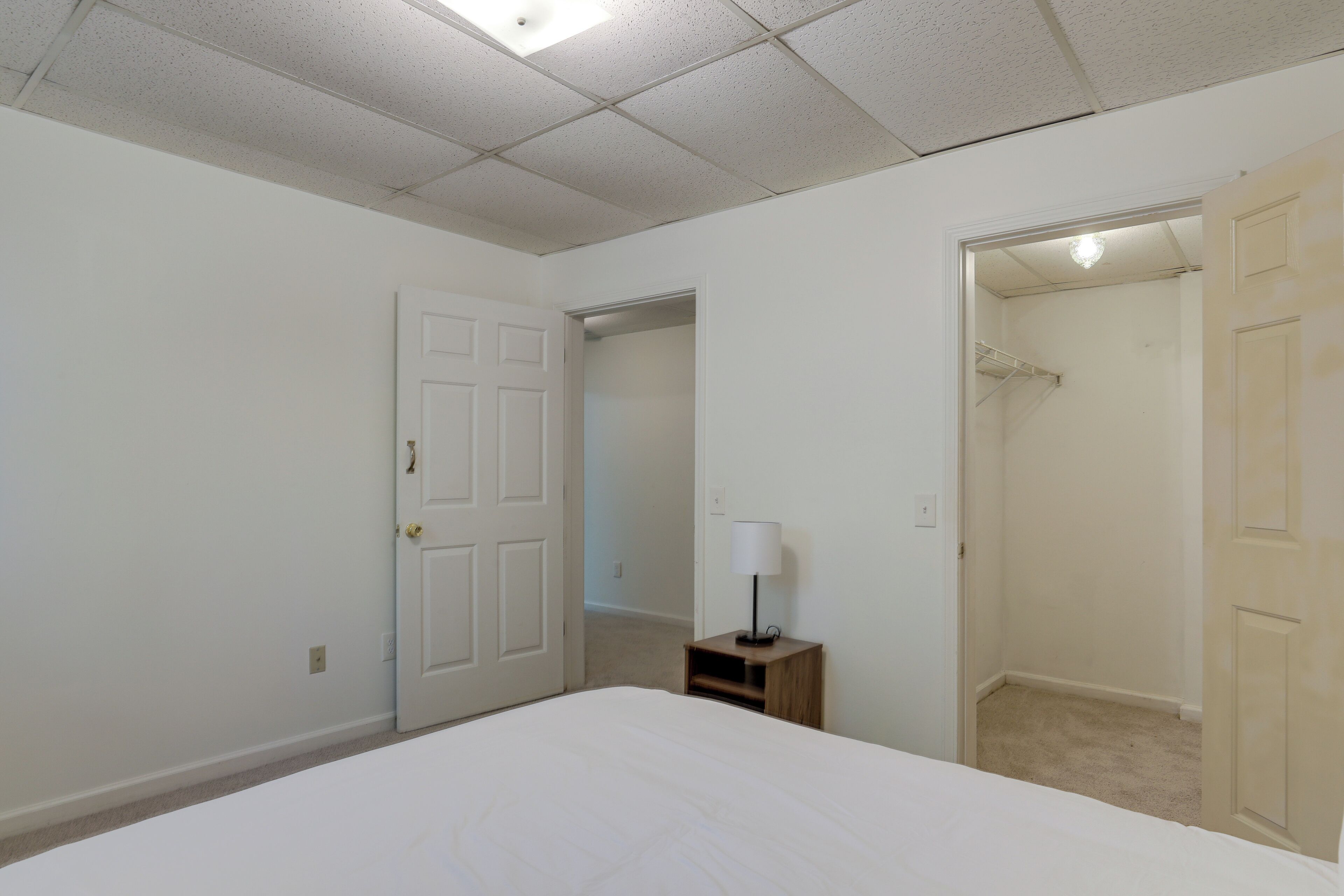A bedroom with a bed, a nightstand with a lamp, and a closet.