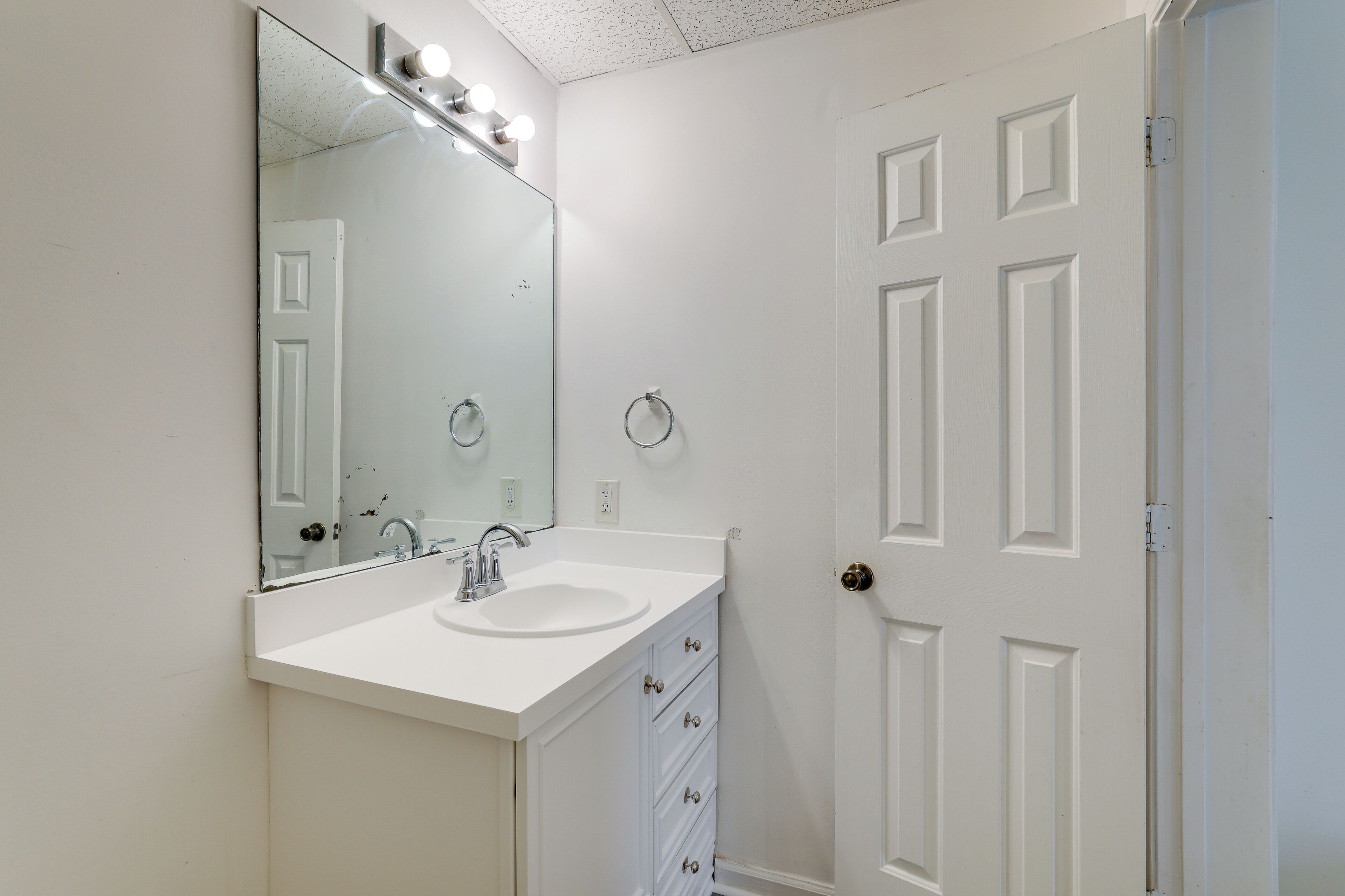 A bathroom with a white sink, a large mirror, and a door with a round doorknob.