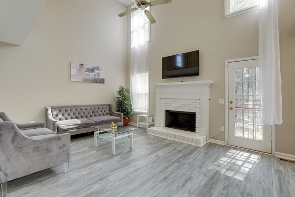 A spacious living room with a fireplace, a flat-screen TV mounted above it, a grey sofa, and a coffee table. - Stone Mountain Vacation Rental With Deck! (Stone Mountain)